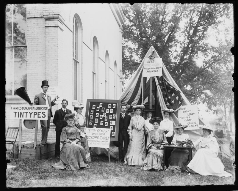 A group sits at a tintype photo booth at a county fair in a photo from 1903.